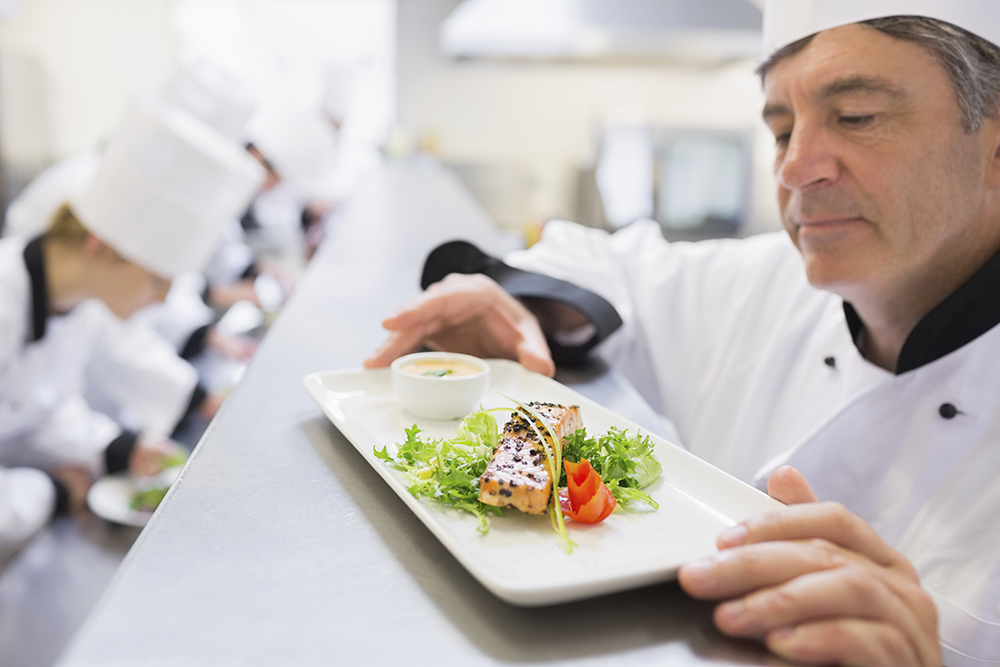 Head ched examing salmon dish as other chefs are preparing other dishes